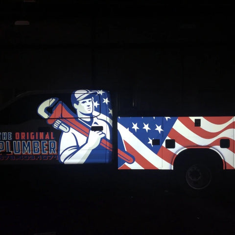 Plumbing service truck wrap photographed at night, reflective film lit by headlights
